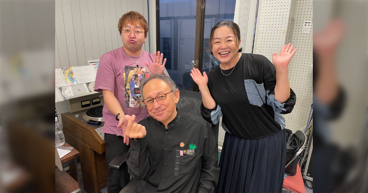 玉城デニー知事、喪服のままラジオ出演し笑顔で指ハート
